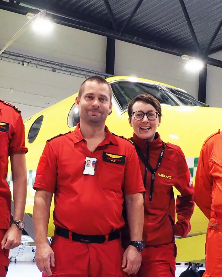 Ansatte foran ambulansefly inne i hangaren